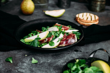 Parma, pear and spinach salad on black plate
