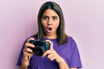 Young latin woman using reflex camera afraid and shocked with surprise and amazed expression, fear and excited face.