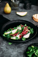 Parma, pear and spinach salad on black plate