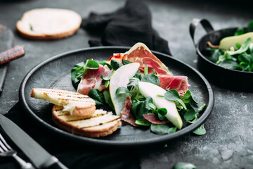 Parma, pear and spinach salad on black plate