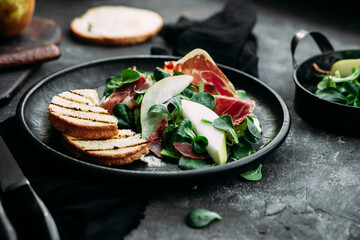 Parma, pear and spinach salad on black plate
