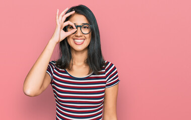 Beautiful asian young woman wearing casual clothes and glasses doing ok gesture with hand smiling, eye looking through fingers with happy face.