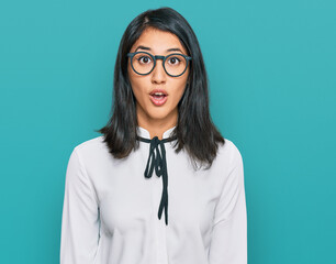 Beautiful asian young woman wearing business shirt and glasses scared and amazed with open mouth...