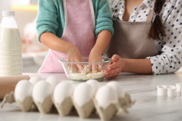 Mother and daughter making dough at table in kitchen, closeup