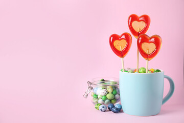 Cup with different candies on pink background, space for text