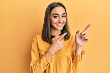 Young brunette girl wearing casual clothes smiling and looking at the camera pointing with two hands and fingers to the side.