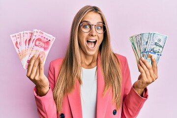 Young blonde woman wearing business style holding yuan chinese banknotes and dollars celebrating crazy and amazed for success with open eyes screaming excited.