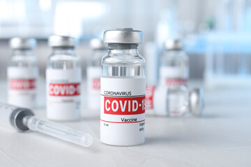 Glass vials with COVID-19 vaccine and syringe on light table