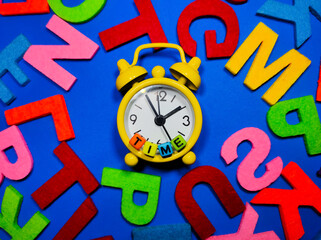 Selective focus.Alarm clock with word TIME and colorful word on blue background.Shot were noise and film grain.
