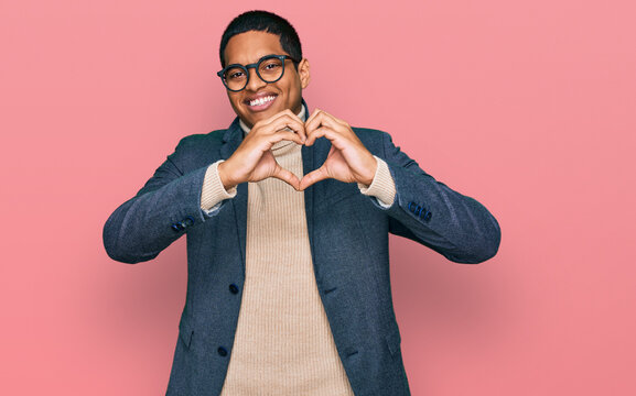 Young handsome hispanic man wearing business jacket and glasses smiling in love showing heart symbol and shape with hands. romantic concept.