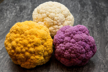 Three whole colorful Cauliflowers. Purple, Gold and White on a slate work top