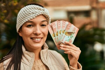 Young latin woman smiling happy holding new zealand dollars at the city.