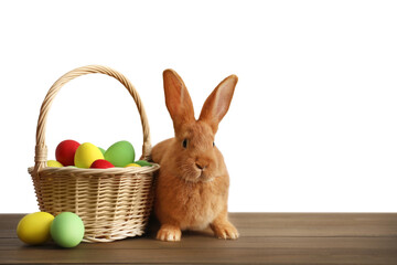 Cute bunny and basket with Easter eggs on wooden table against white background. Space for text