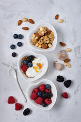 trio of heart-shaped bowls arranged on a slightly textured background with berries, dried fruit, white yogurt, wholemeal flakes and honey