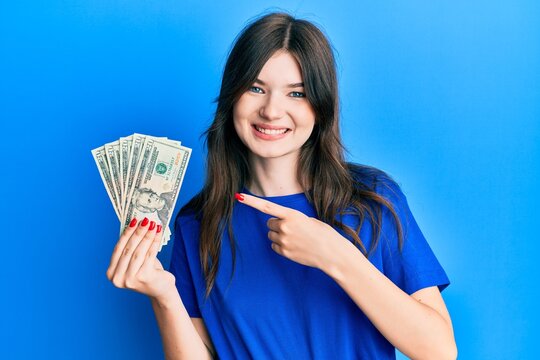 Young beautiful caucasian girl holding 20 dollars banknote smiling happy pointing with hand and finger