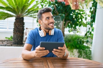 Fototapeta premium Young hispanic man smiling happy using tablet and headphones at the terrace.