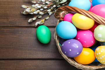 Fototapeta na wymiar Colorful Easter eggs in wicker basket and willow branches on wooden table, flat lay. Space for text
