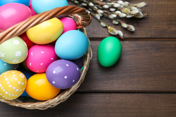 Fototapeta na wymiar Colorful Easter eggs in wicker basket and willow branches on wooden table, flat lay. Space for text