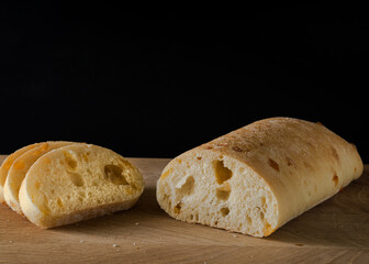 Ciabatta - Italian bread with cheese cut into slices on a wooden board on a black background