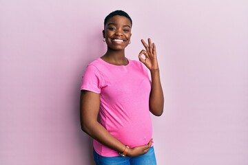 Young african american woman expecting a baby, touching pregnant belly smiling positive doing ok sign with hand and fingers. successful expression.