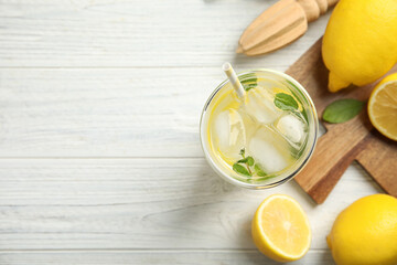 Cool freshly made lemonade, reamer and fruits on white wooden table, flat lay. Space for text