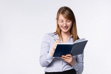 Blonde sensual businesswoman wearing classic gray shirt and glasses, making notes in diary book, writing plans, business events, inspired, happy. Gray background, side space