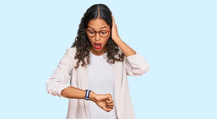 Young african american girl wearing business clothes looking at the watch time worried, afraid of...