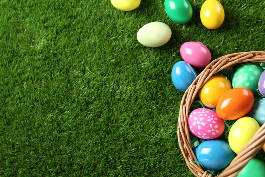 Wicker basket with Easter eggs on green grass, flat lay. Space for text