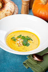 Pumpkin soup in a white plate filmed in decor