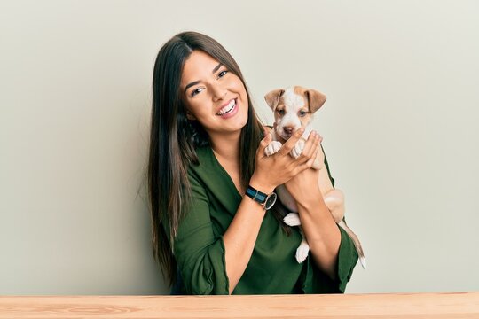 Young hispanic girl smiling happy and hugging dog sitting on the table over isolated white background.