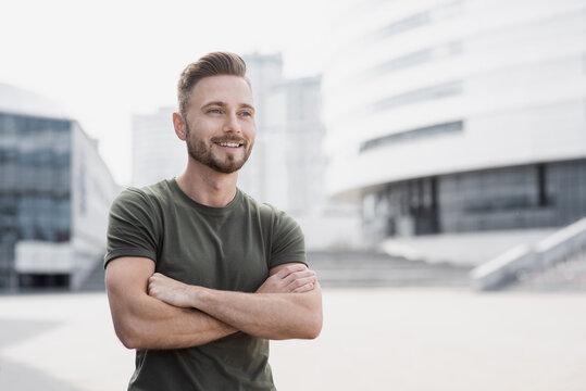 Handsome smiling young man portrait. Cheerful men with crossed arms looking away on city street. People, male beauty concept