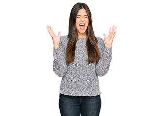 Young brunette woman wearing casual winter sweater celebrating mad and crazy for success with arms raised and closed eyes screaming excited. winner concept