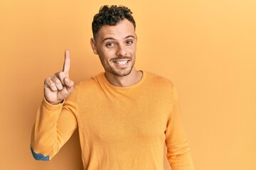 Fototapeta premium Young hispanic man wearing casual clothes smiling with an idea or question pointing finger up with happy face, number one
