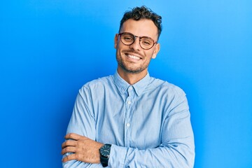 Young hispanic man wearing casual clothes and glasses happy face smiling with crossed arms looking...