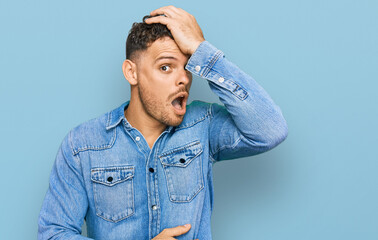 Young hispanic man wearing casual denim jacket surprised with hand on head for mistake, remember...