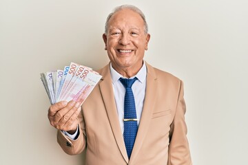 Senior caucasian man holding swedish krona banknotes looking positive and happy standing and smiling with a confident smile showing teeth