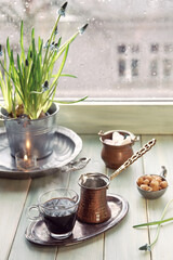 Oriental coffee in traditional copper coffee pot with flowers on window sill. Wooden windowsill with hyacinth flower pot. Cold rainy day in spring. Cozy scene, hygge concept.