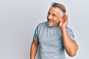 Middle age grey-haired man wearing casual clothes smiling with hand over ear listening and hearing to rumor or gossip. deafness concept. - obrazy, fototapety, plakaty
