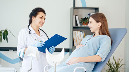 Obraz premium Happy Pregnant Woman Visit Gynecologist Doctor at the Medical Clinic. Female Doctor Examine Pregnant Young Mother to Check Up Her Healthcare. Teenage Pregnancy. Consulting of Pregnant at Clinic.