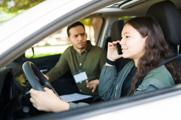 Teenage girl calling a friend on the phone while taking a driving test