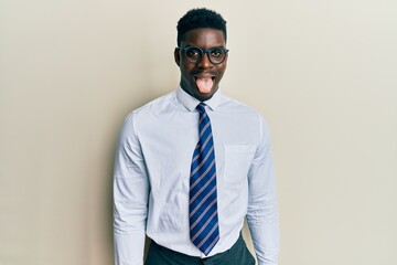 Handsome black man wearing glasses business shirt and tie sticking tongue out happy with funny expression. emotion concept.