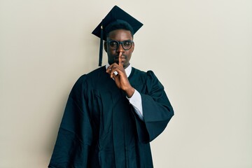 Handsome black man wearing graduation cap and ceremony robe asking to be quiet with finger on lips. silence and secret concept.