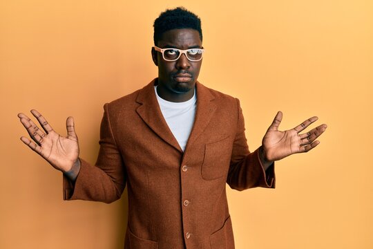 Handsome black man wearing elegant clothes and glasses clueless and confused with open arms, no idea and doubtful face.
