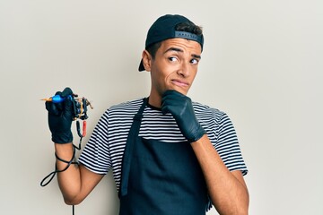 Young handsome african american man tattoo artist wearing professional uniform and gloves holding tattooer machine thinking worried about a question, concerned and nervous with hand on chin