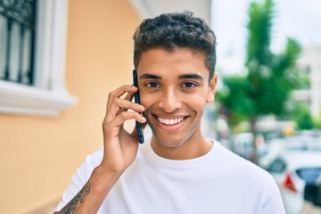 Young latin man smiling happy talking on the smartphone walking at the city.
