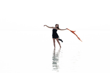 Beautiful woman on the beach, attractive slim model wearing black dress and dancing with a scarf, enjoying summer holidays. Sea, coast, woman and water reflection 