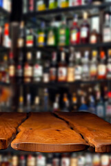 Wooden board on a background of bottles with alcohol. Old bar counter as layout for design. Workpiece for design. Empty place to advertise products. Blurred interior of the bar in the background.