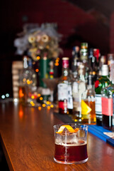Yellow cocktail on bar counter. Whiskey, rum or brandy on the background of bottles with alcohol. Glass with booze on a wooden board.