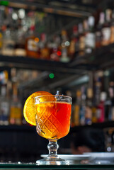 Orange cocktail on the bar. Mulled wine with white wine. Shelves with bottles of alcohol blurred in the background.
