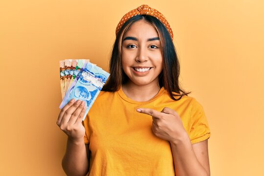 Young latin woman holding canadian dollars smiling happy pointing with hand and finger